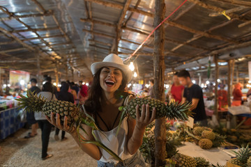 Wall Mural - Cheerful Girl Hold Pineapples Shopping On Tropical Street Market In Thailand Young Woman Tourist Buying Fresh Fruits On Asian Bazaar