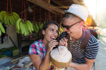 Wall Mural - Happy Couple Drinking One Coconut On Thailand Street Market, Cheerful Tourists Man And Woman Young In Traditional Fruits Bazaar In Asia Exotic Vacation Concept