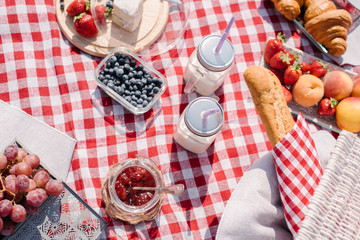 Wall Mural - Picnic in the nature with croissants, peaches, strawberries, blueberries, grapes, baguette, cheese and glass bottles of milk