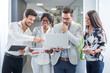 © Bojan - Multiethnic group of inspired young people standing and discussing new project on laptop in office building.