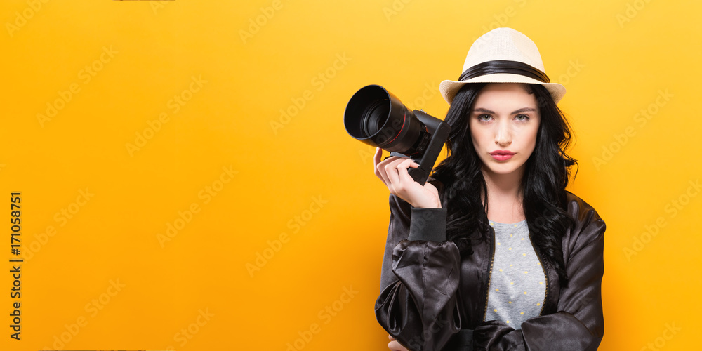  Young woman holding a camera on a yellow background - obrazy, fototapety, plakaty 