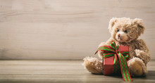 Teddy Bear Holdimg A Gift On A Wooden Floor
