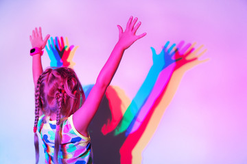 Girl stands at the wall with her hands up, on which her silhouette is reflected in different colors. Back view