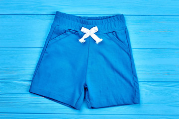 Wall Mural - Blue cotton kids shorts. Baby boy casual textile short pants on blue wooden background. Summer apparel for little boys.