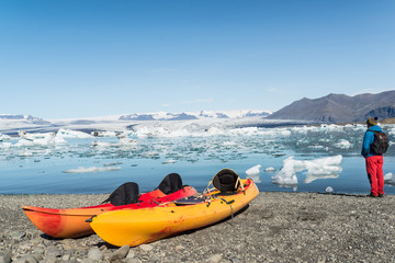 Hombre joven al lado de dos kayaks en la orilla del lago glaciar Jokulsarlon. Islandia