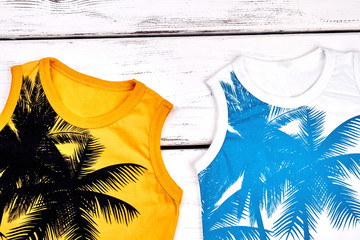 Kids new cute sleeveless t-shirts. Summer trendy palm tree print t-shirts for kids, wooden background. New kids apparel on sale. Kids boutique fashion.