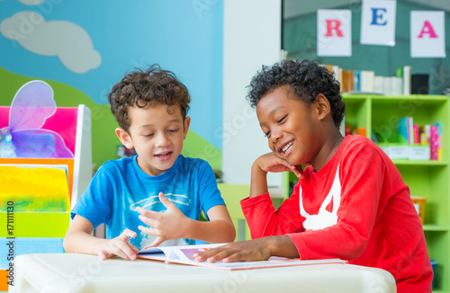 Plakat Dwa chłopiec dzieciak siedzi na stołowej i czytelniczej bajki książce w preschool bibliotece, dzieciniec edukaci szkolnej pojęcie