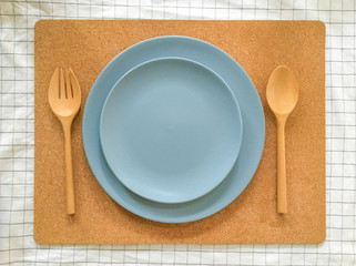 Top view of two empty blue plate with wooden fork and spoon on wood background