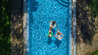 © Iuliia Sokolovska - Aerial top view of family in swimming pool from above, happy mother and kids swim on inflatable ring donuts and have fun in water on family vacation