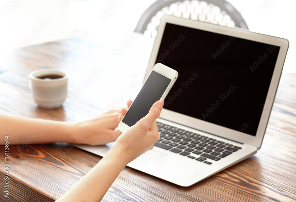 Young woman using mobile phone and laptop for searching information in internet at table