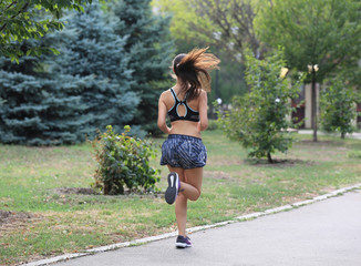 Young sporty woman running in green park