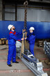 © Evgeniy Kalinovskiy - Workers at the plant load the cargo onto the hook of the crane against the background of production