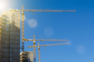 High cranes on the construction of residential buildings, against the blue sky