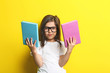 Beautiful little girl with glasses and books on yellow background