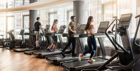 group of four people, men and women, running on treadmills in modern and luminous fitness gym