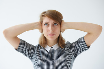 Wall Mural - Annoyed and stressed angry young Caucasian woman wearing checkered dress looking up and covering her ears with hands because of unpleasant disturbing noise coming from her neighbours upstairs