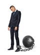 © gearstd - A sad businessman looks down while shackled to a large iron ball with a chain to his ankle.