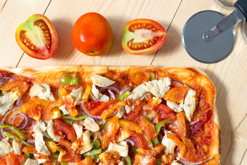 Home made pizza, tomatoes and pizza cutting knife on wood surface