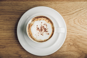 Wall Mural - Top view of hot cappuccino in white coffee cup on brown wood table near window in morning,vintage filtered,