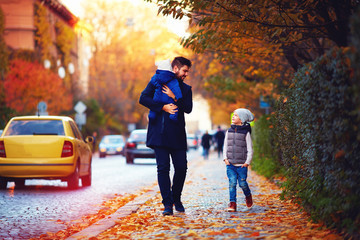 father with kids walking along autumn city street