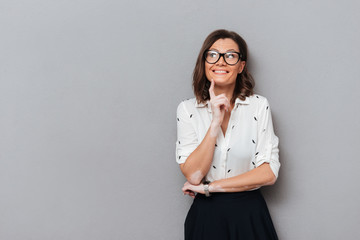 happy pensive woman in eyeglasses and business clothes holding finger