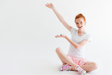 Wall Mural - Happy ginger woman girl sitting on floor and showing something