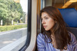 © papa - The young woman sadly looking out the window sitting inside the train car.