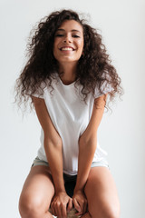 Wall Mural - Happy cheerful girl with curly hair sitting on a chair