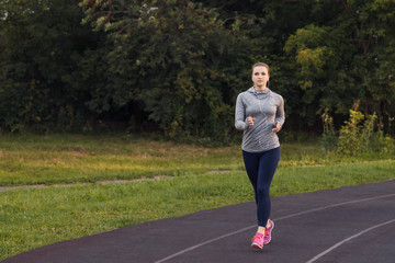 Pretty sporty woman running at park in sunrise