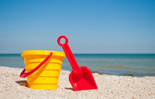 Yellow Childrens Bucket With Red Toy Toy Plastic Red Scapula On The Left Against The Blue Sea And Blue Sky Yellow Sand Beach Sea Shore Seashells Summer Vacation Sunny Summer Day, Bright Sun, Baby Toys