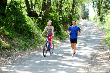 Wall Mural - young woman riding bicycle beside a young man running in countryside in summer