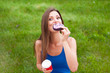Cheerful young woman taking a bite of the donut and holds a coffee Cup outdoors
