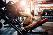 © ZaStock - Man Using A Press Machine In A Fitness Club. Strong man doing an exercise on its feet in the simulator. Side view