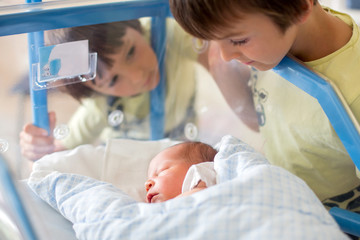 Sticker - Beautiful newborn baby boy, laying in crib in prenatal hospital, his brothers looking at him