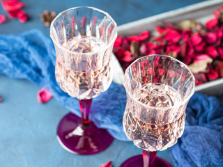 Two stemmed champagne glasses on blue textured background with pink dried flowers. Valentine's day wedding romantic date invitation