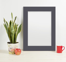 Mock up of blank photo frame with plant pot, mug and apple on wooden shelf.