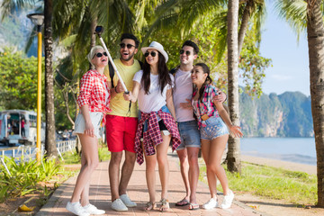 Wall Mural - people group take selfie with action camera on stick while walking in palm tree park on beach, happy