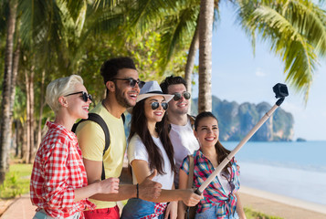 Wall Mural - people group take selfie with action camera on stick while walking in palm tree park on beach, happy