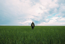 Rear View Of Man Standing On Grassy Field Against Cloudy Sky