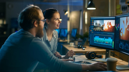 Beautiful Female and Handsome Male Video Editors Discuss Footage They're Working On. They Enjoy Working Together in a Cozy Creative Studio.