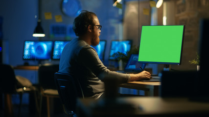 Poster - Creative Bearded Man Works on a Personal Computer with Isolated Mock-up Green Screen. He Works Alone in the Office Late at Night.