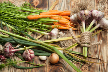 Fresh vegetables, garlic, carrots and onions on a rustic wooden background. View from above.