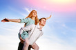 © cezarksv - Young guy piggybacking cheerful girlfriend like airplane on the background of sky