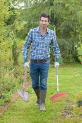 smiling man in hat holding shovel and hoe