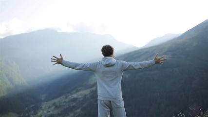 man raises hands up standing back on mountain top morning sun shine slow motion. no face male silhou