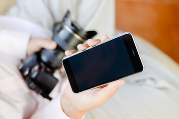 Man using mobile phone and holding DSLR camera in hand on background indoors