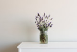 Fototapeta Lawenda - Lavender in glass jar on white cabinet against neutral wall background