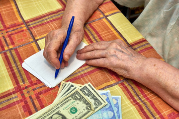 An elderly woman writes down expenses in notepad