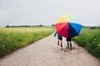 © sally anscombe/Stocksy - Children walking on a rainy day with a rainbow umbrella