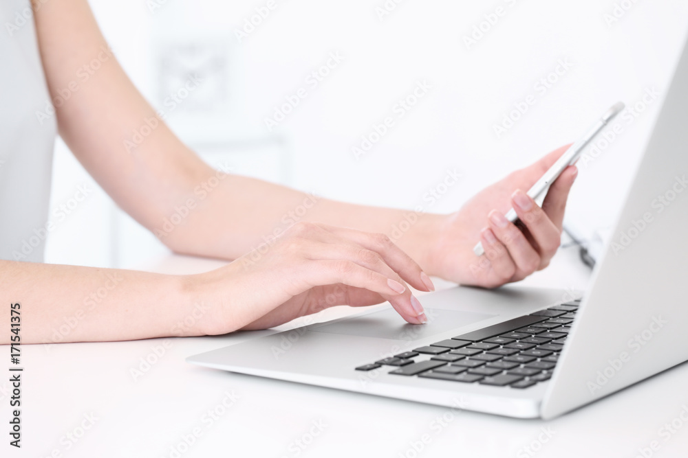 Young woman using mobile phone and laptop for searching information in internet at table